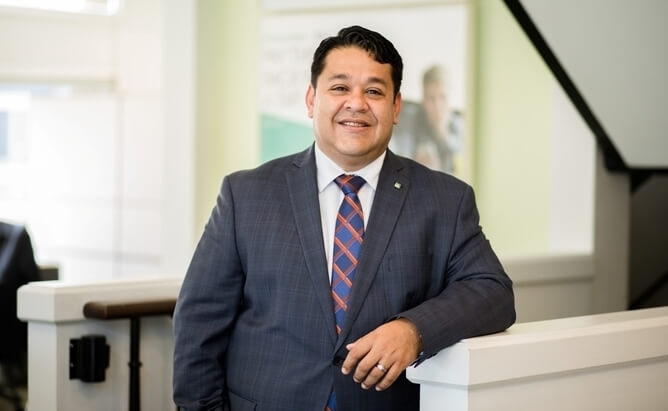 Omar wearing a dark gray business suit and smiling